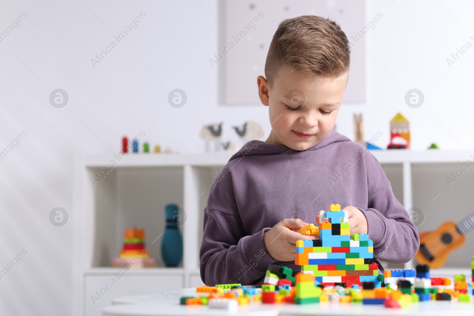 Photo of Cute boy playing with building blocks at white table indoors. Space for text