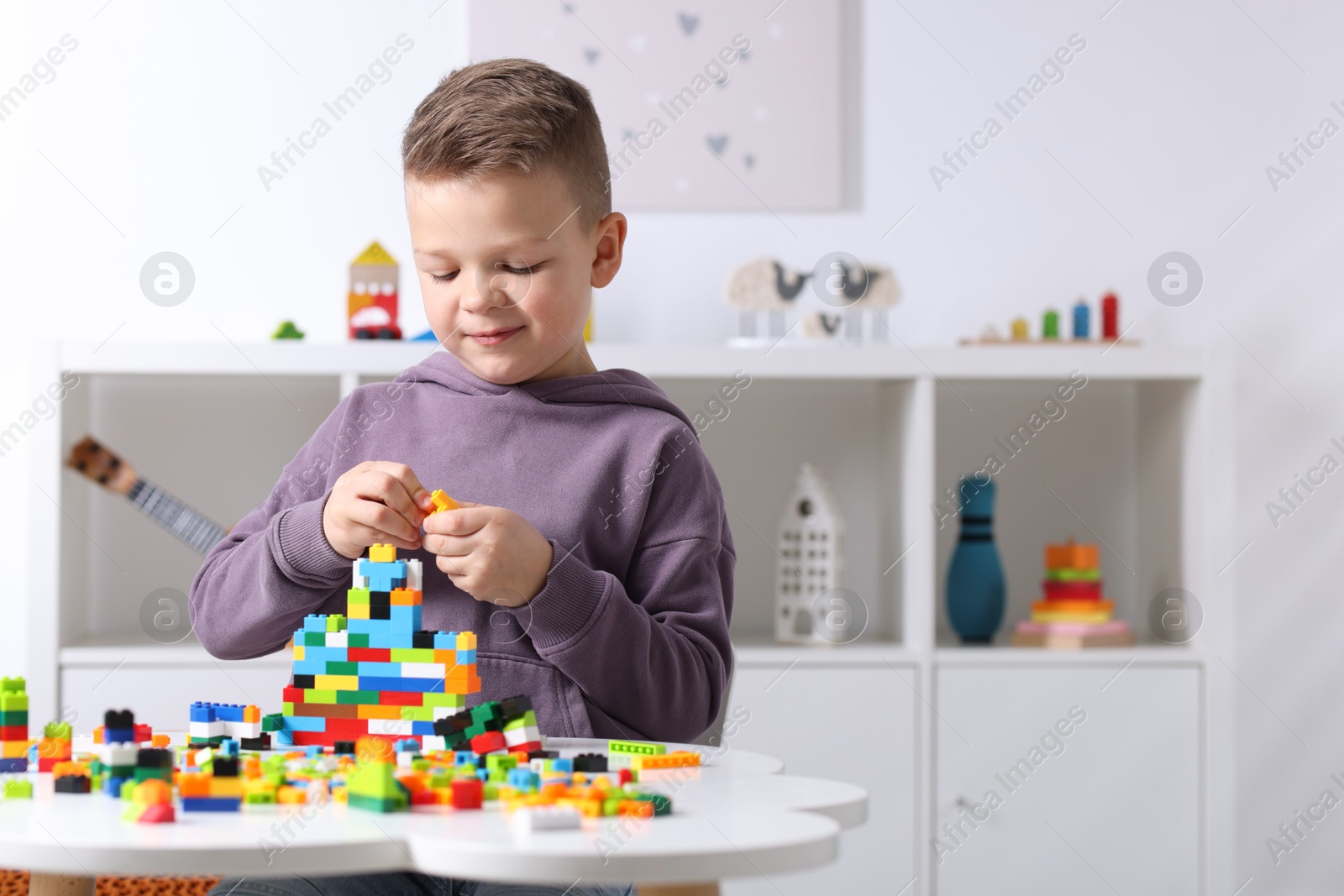 Photo of Cute boy playing with building blocks at white table indoors. Space for text