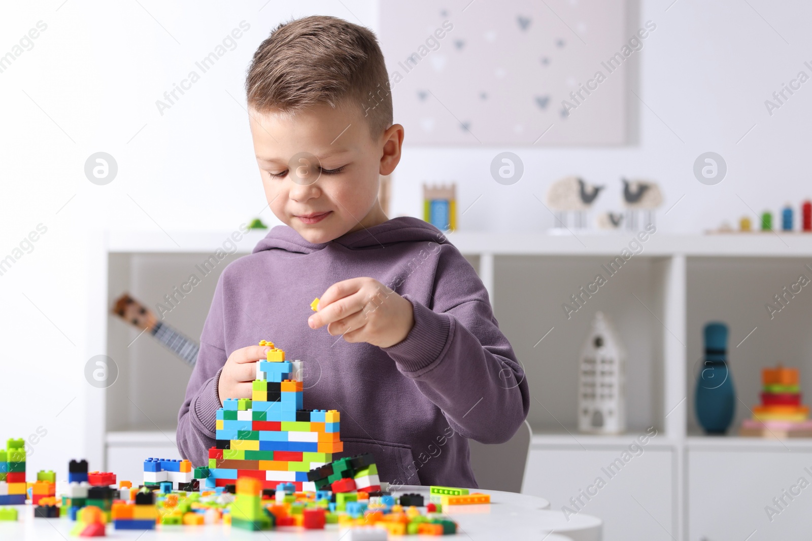 Photo of Cute boy playing with building blocks at white table indoors. Space for text