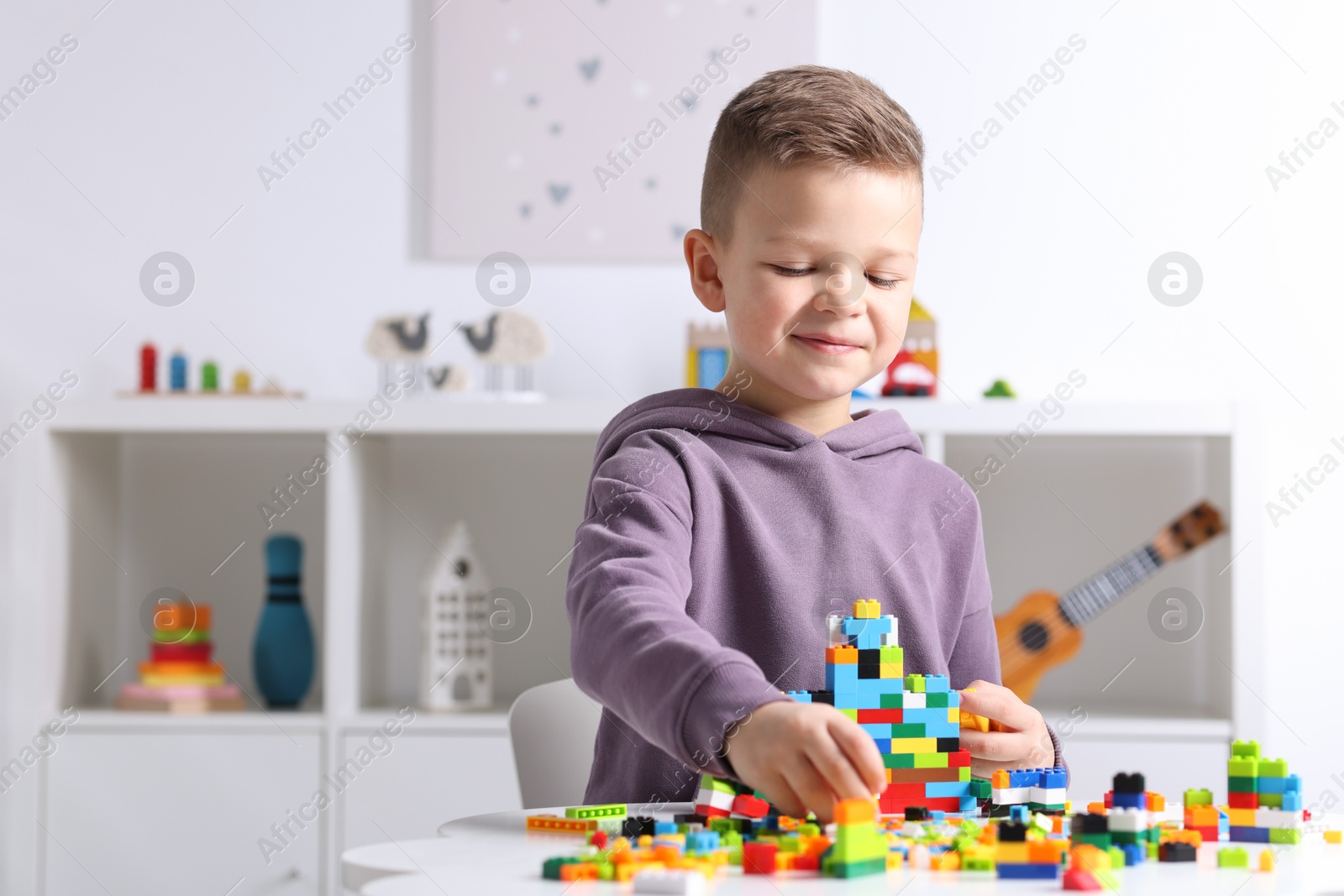 Photo of Cute boy playing with building blocks at white table indoors. Space for text