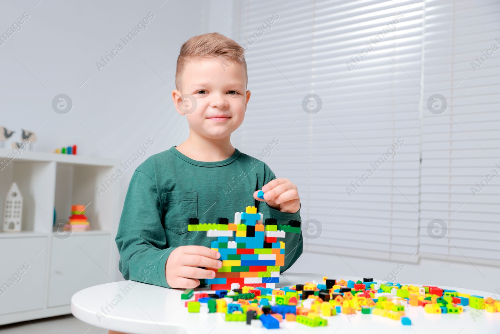 Photo of Cute boy playing with building blocks at white table indoors. Space for text