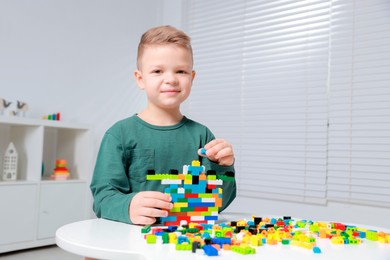 Photo of Cute boy playing with building blocks at white table indoors. Space for text