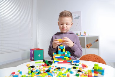 Photo of Cute boy playing with building blocks at white table indoors. Space for text