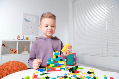 Photo of Cute boy playing with building blocks at white table indoors. Space for text