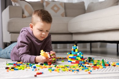 Photo of Cute boy playing with building blocks on floor at home. Space for text