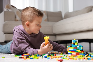 Photo of Cute boy playing with building blocks on floor at home. Space for text