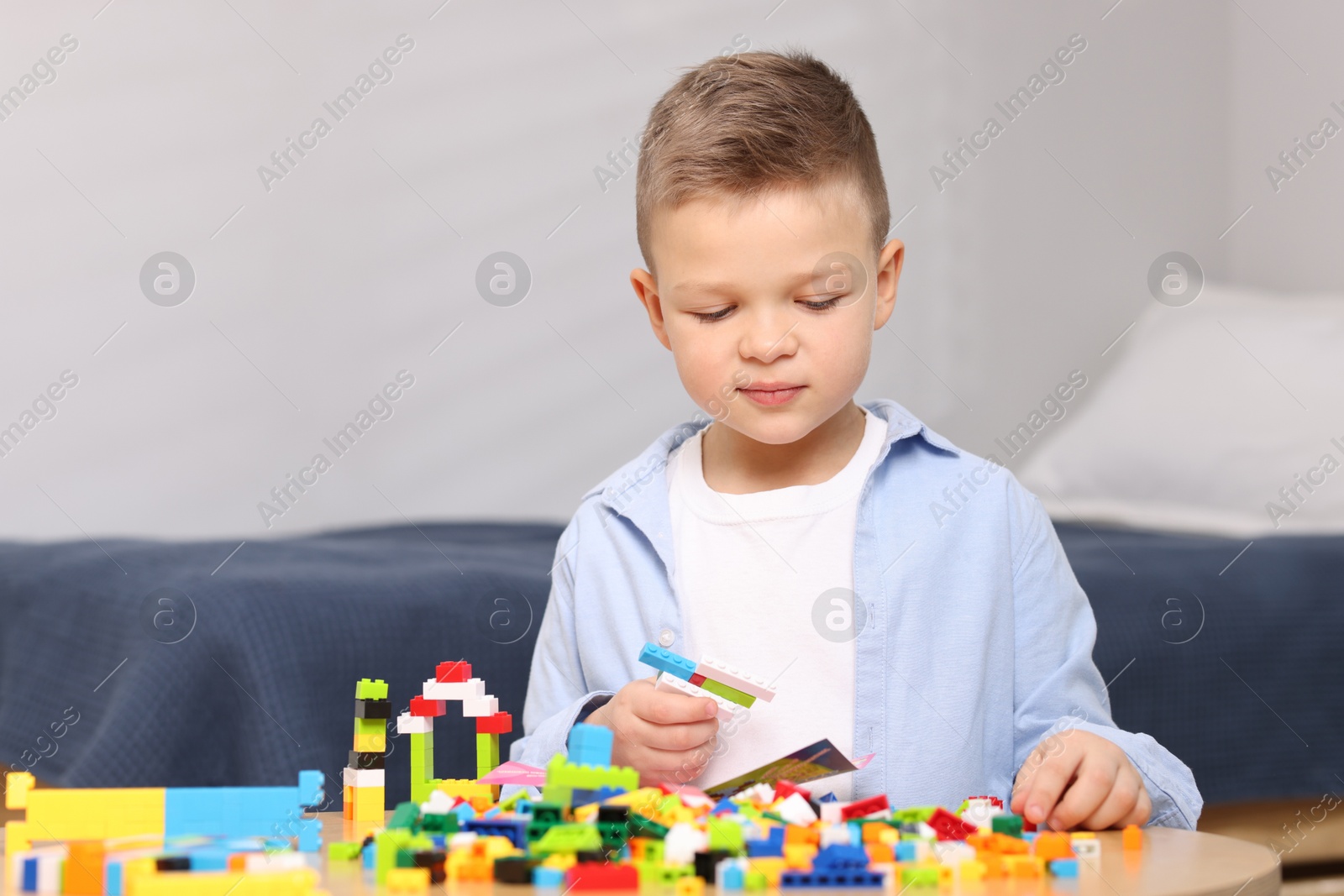 Photo of Cute boy playing with building blocks at wooden table indoors