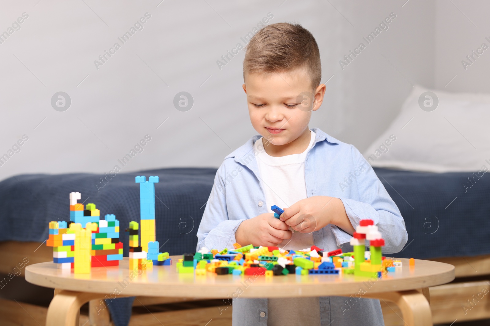 Photo of Cute boy playing with building blocks at wooden table indoors