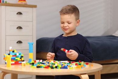 Photo of Cute boy playing with building blocks at wooden table indoors