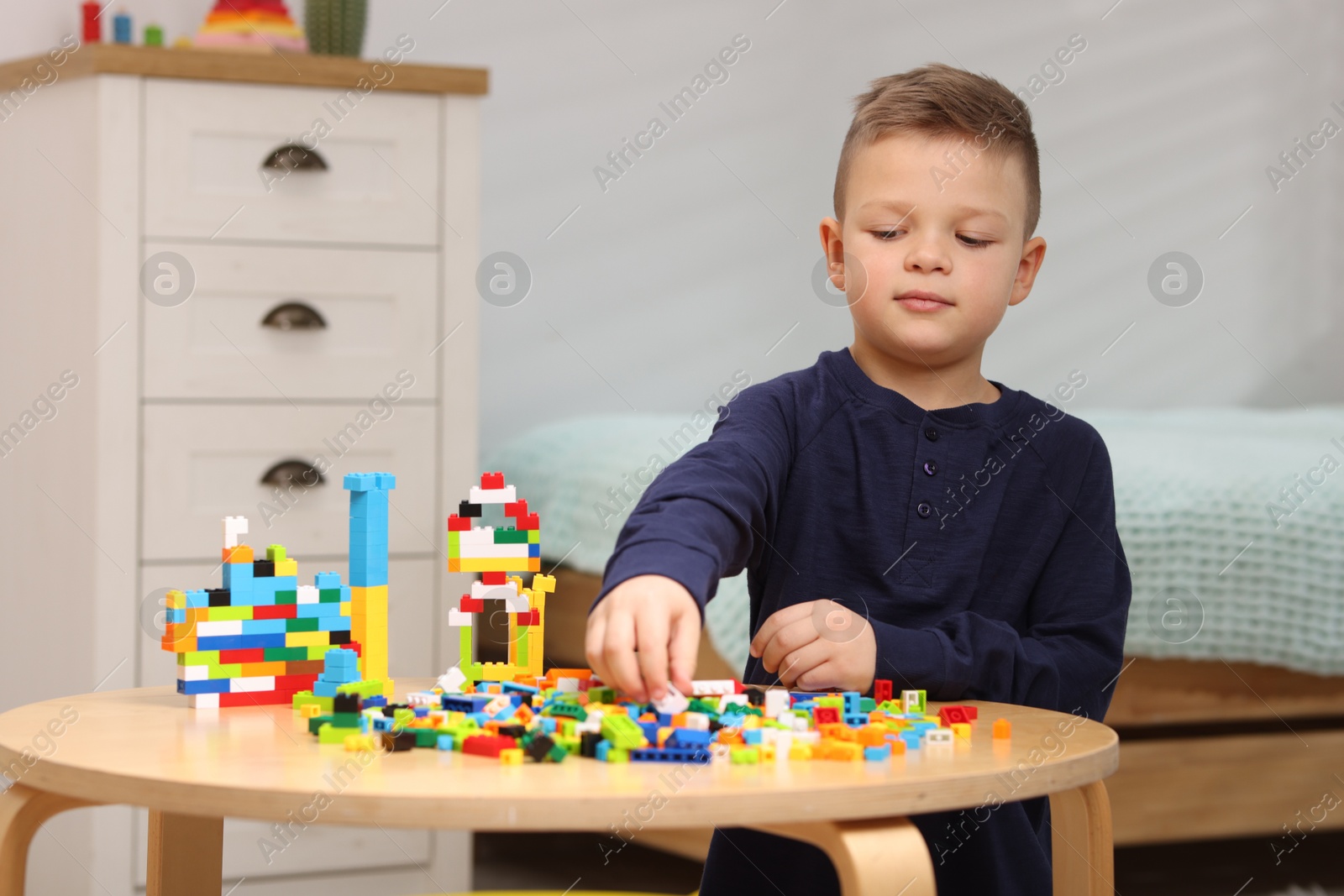 Photo of Cute boy playing with building blocks at wooden table indoors