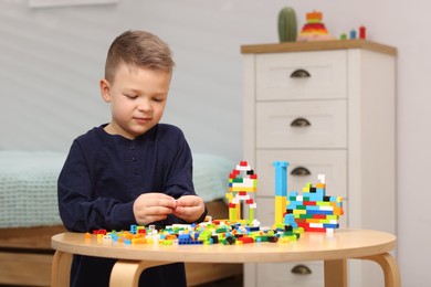 Photo of Cute boy playing with building blocks at wooden table indoors