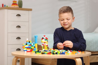 Photo of Cute boy playing with building blocks at wooden table indoors