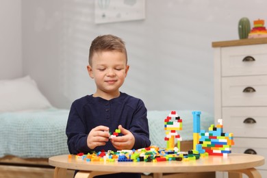 Photo of Cute boy playing with building blocks at wooden table indoors