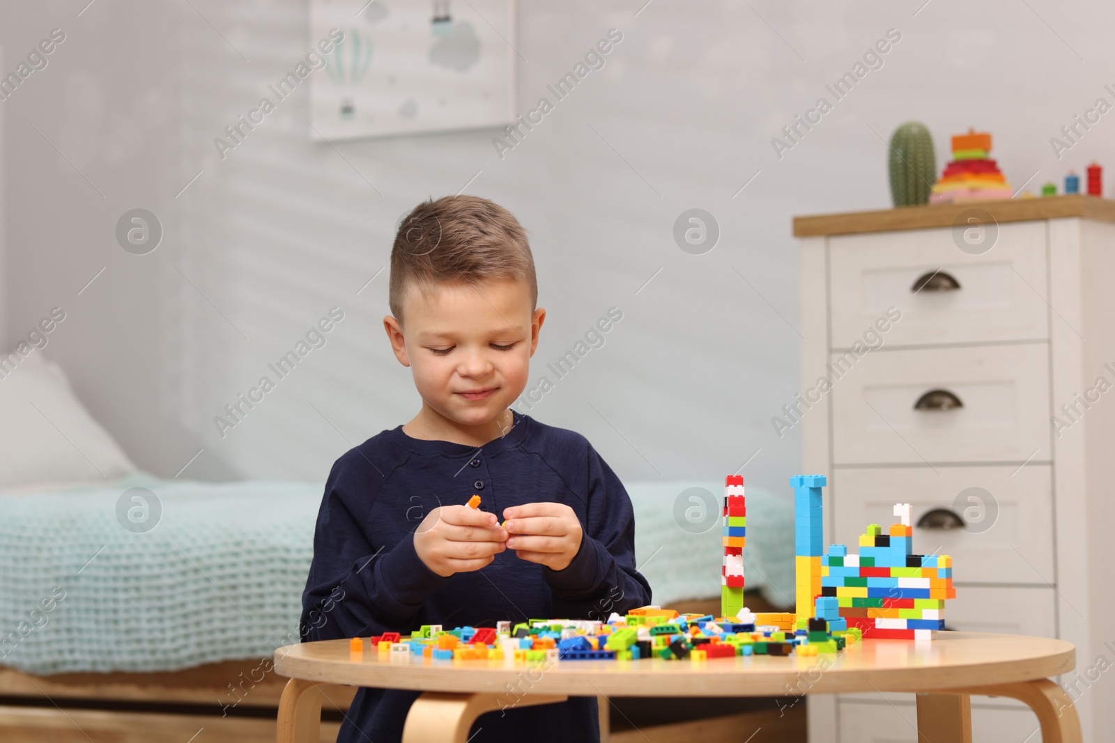 Photo of Cute boy playing with building blocks at wooden table indoors