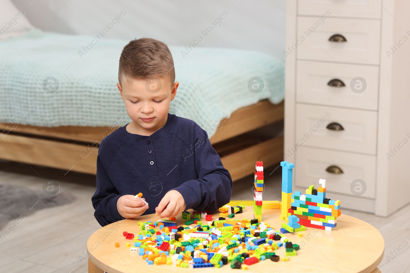 Photo of Cute boy playing with building blocks at wooden table indoors