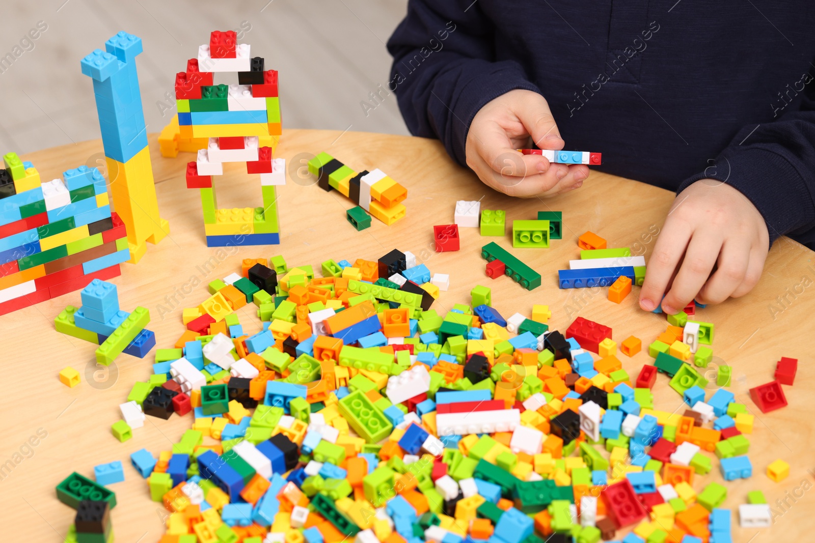 Photo of Cute boy playing with building blocks at wooden table indoors, closeup