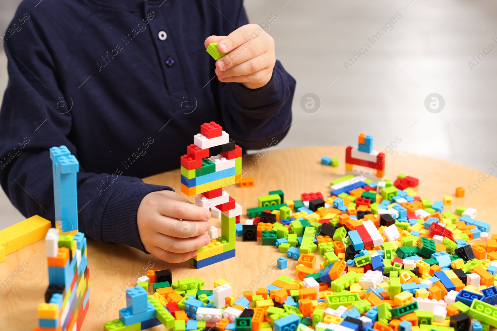 Photo of Cute boy playing with building blocks at wooden table indoors, closeup