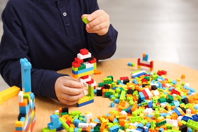 Photo of Cute boy playing with building blocks at wooden table indoors, closeup