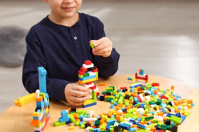 Photo of Cute boy playing with building blocks at wooden table indoors, closeup