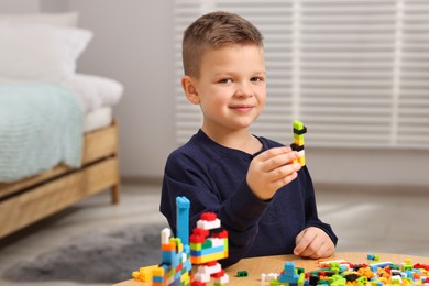 Photo of Cute boy playing with building blocks at wooden table indoors