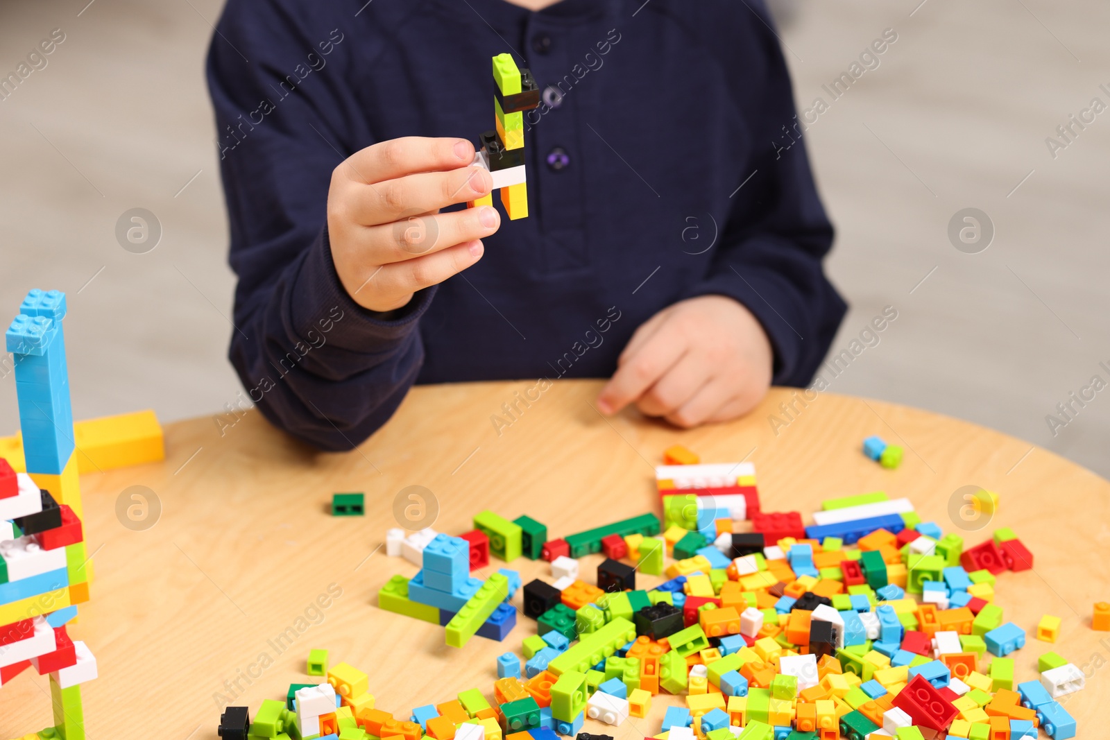 Photo of Cute boy playing with building blocks at wooden table indoors, closeup