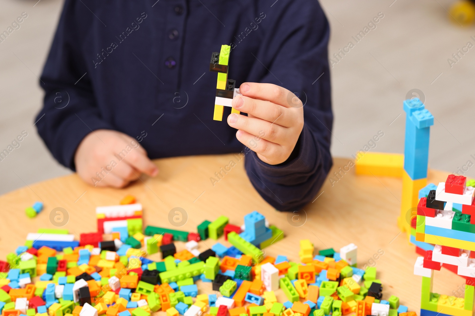 Photo of Cute boy playing with building blocks at wooden table indoors, closeup