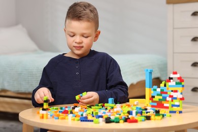 Photo of Cute boy playing with building blocks at wooden table indoors