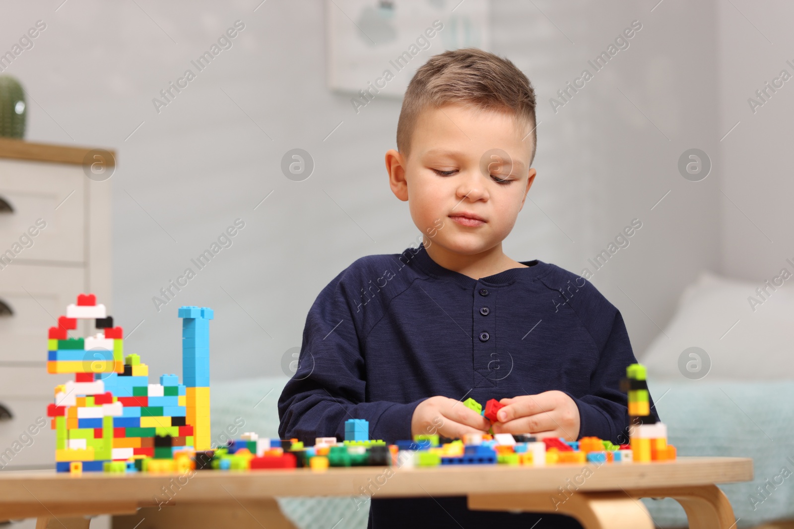 Photo of Cute boy playing with building blocks at wooden table indoors