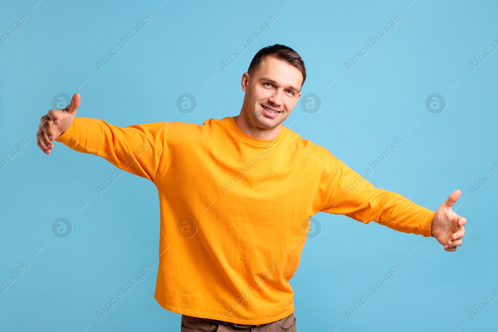 Photo of Cheerful man welcoming guests on light blue background