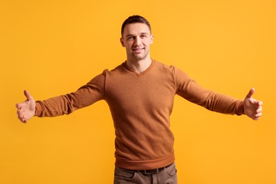 Photo of Cheerful man welcoming guests on orange background