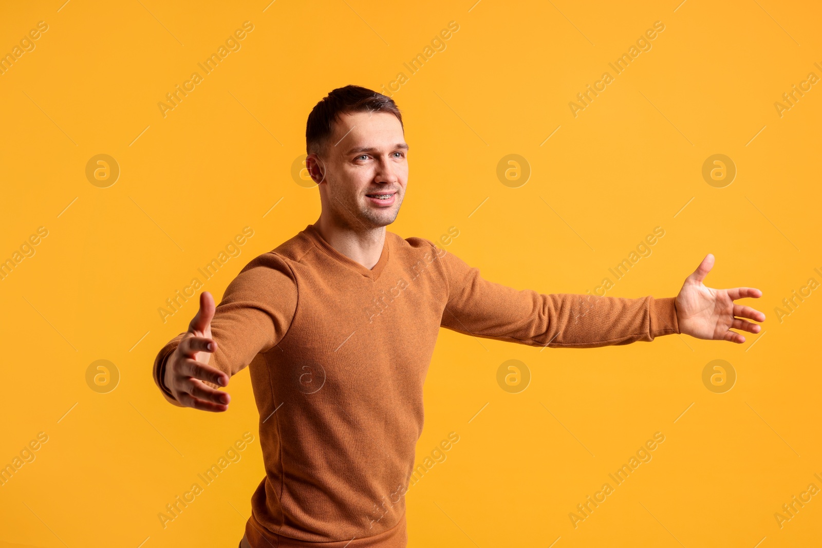 Photo of Cheerful man welcoming guests on orange background