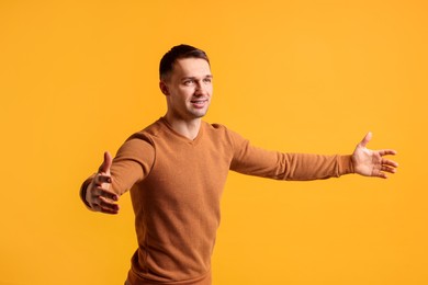 Photo of Cheerful man welcoming guests on orange background