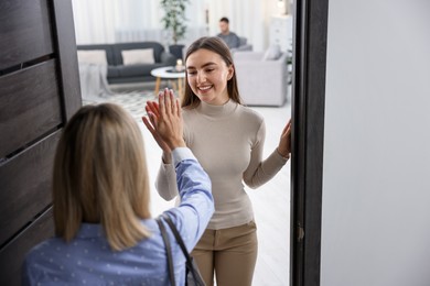 Photo of Happy woman greeting friend and welcoming her to apartment