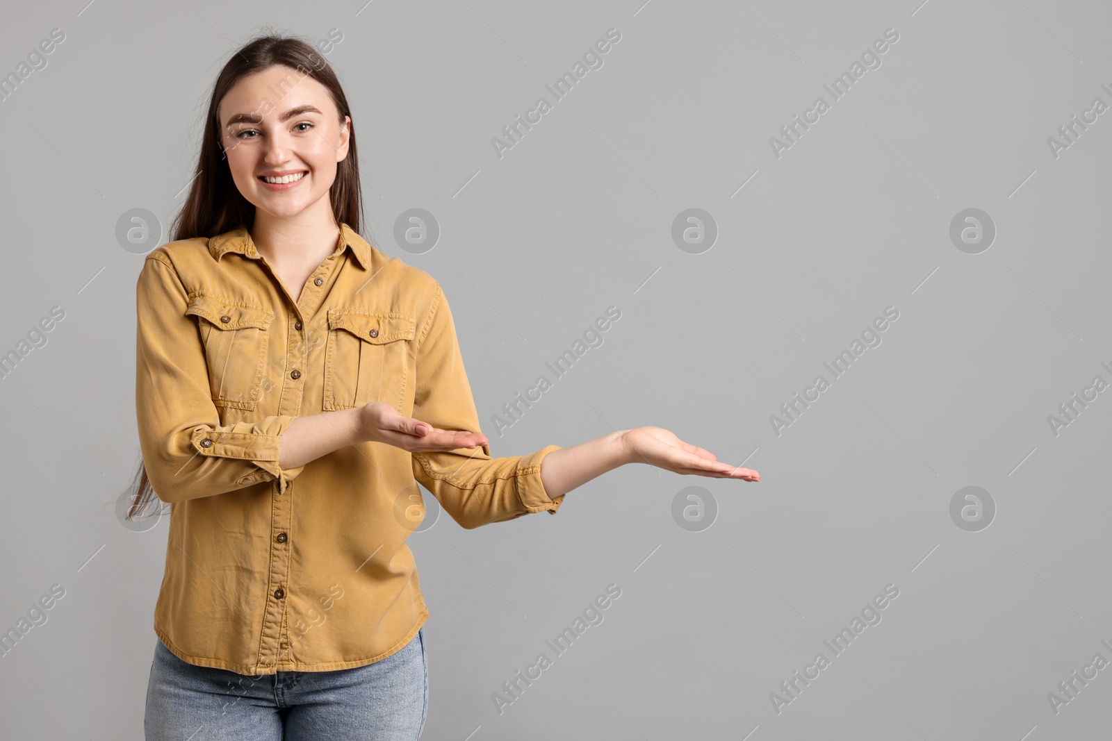 Photo of Woman welcoming friends or guests on grey background. Space for text