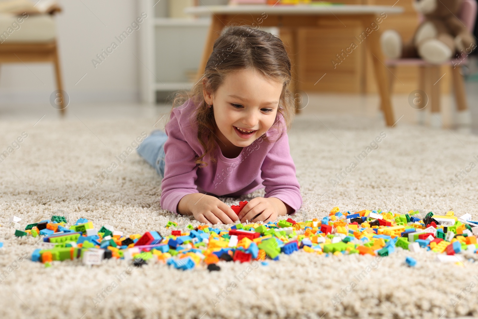 Photo of Cute girl playing with building blocks on floor at home