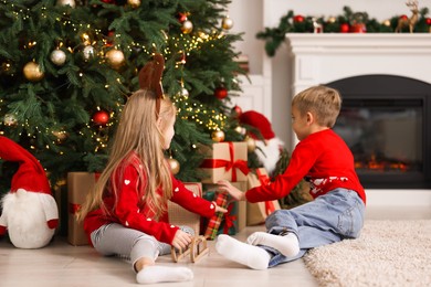 Photo of Little children with gifts near Christmas tree at home