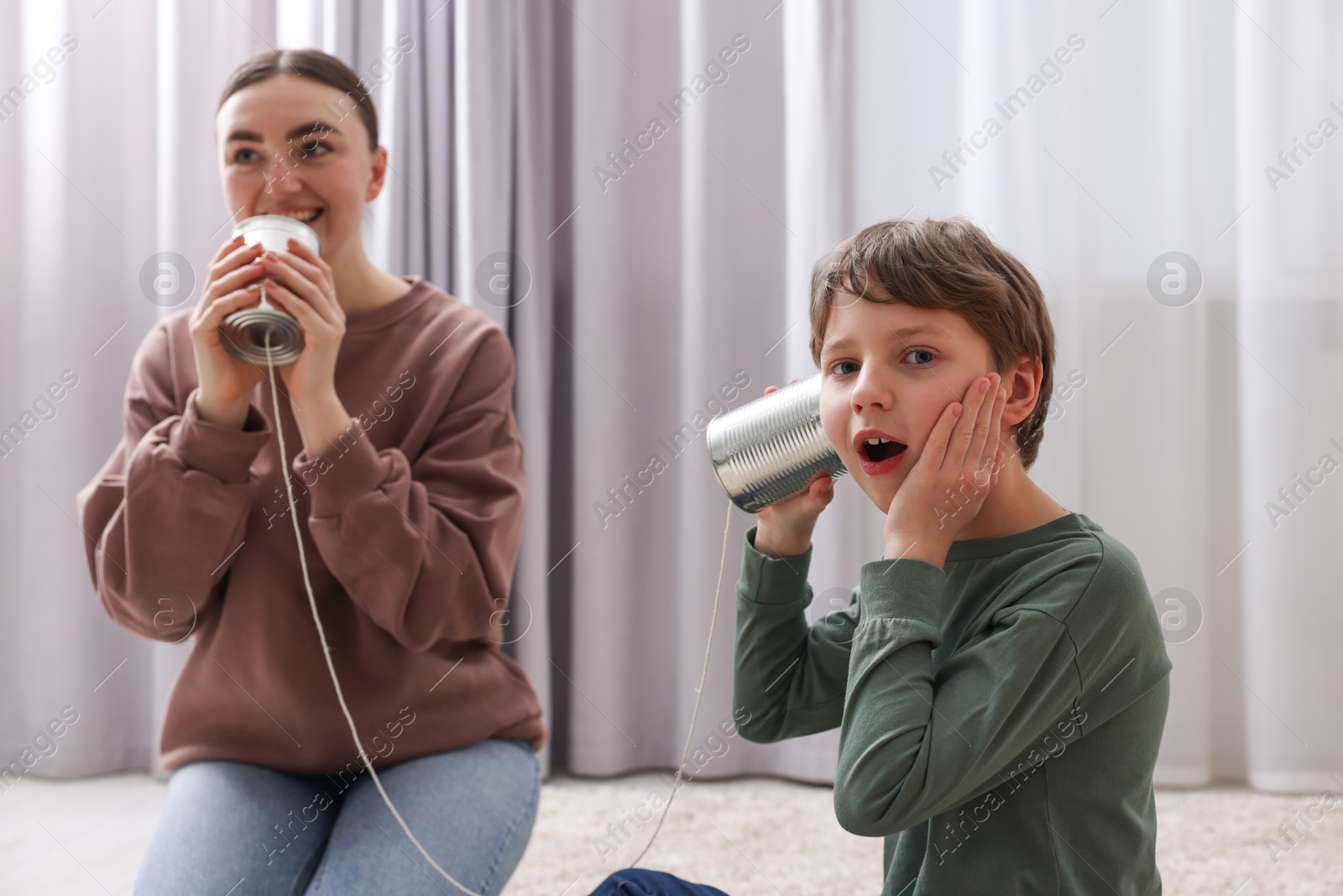 Photo of Woman and boy talking on tin can telephone indoors