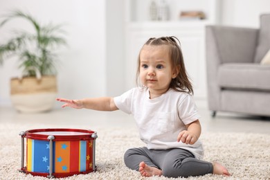 Photo of Cute little girl playing with toy drum on floor at home