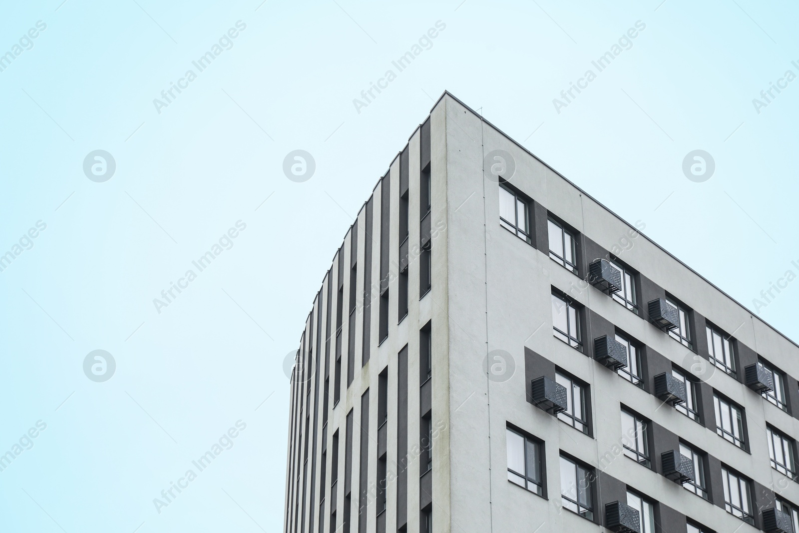 Photo of Modern building with many windows against blue sky, low angle view. Space for text