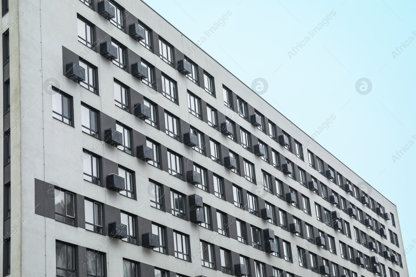 Photo of Modern building with many windows against blue sky, low angle view