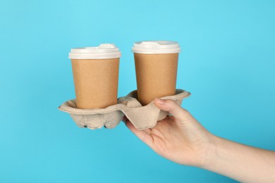 Photo of Woman holding holder with paper cups against light blue background, closeup. Mockup for design