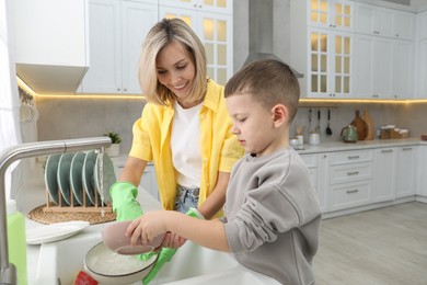 Photo of Little boy helping his mother washing dishes at home