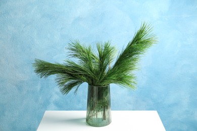 Photo of Beautiful pine tree branches on table near blue wall. Christmas decor