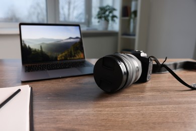 Photo of Professional photo camera, laptop and notepad on wooden desk indoors