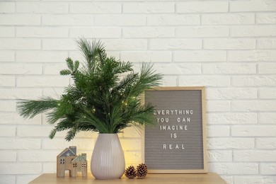 Photo of Beautiful Christmas composition of decorated fir and pine tree branches on wooden table near white brick wall