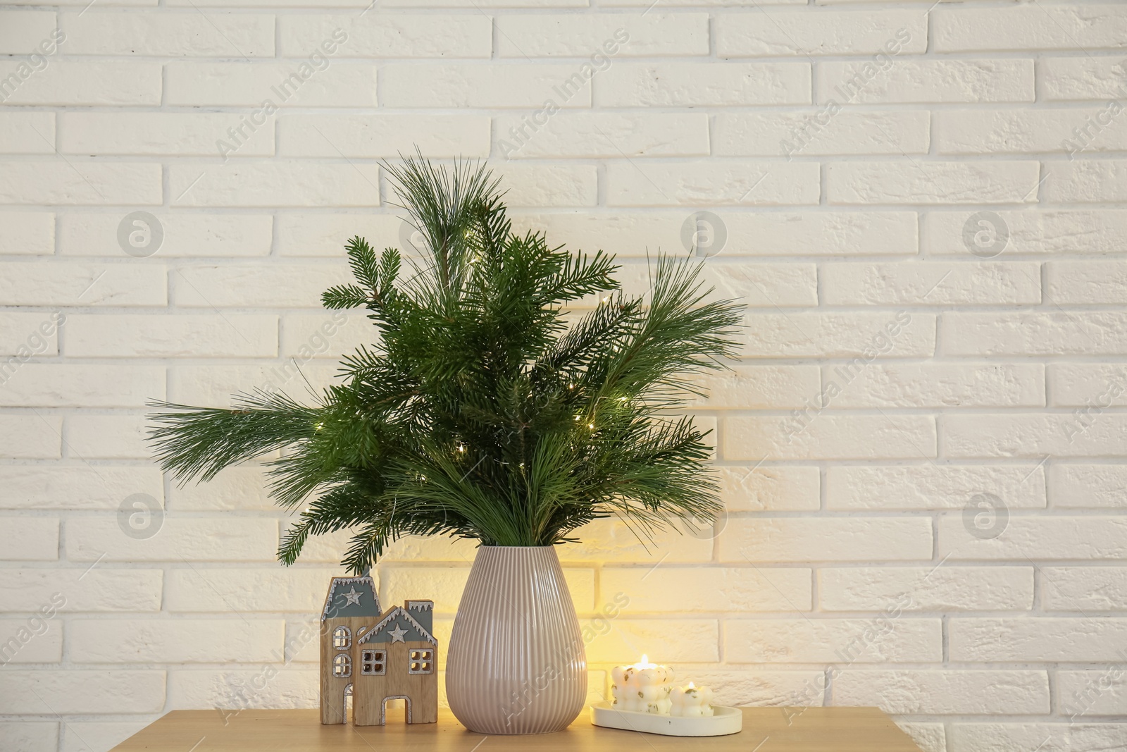 Photo of Beautiful Christmas composition of decorated fir and pine tree branches on wooden table near white brick wall, space for text