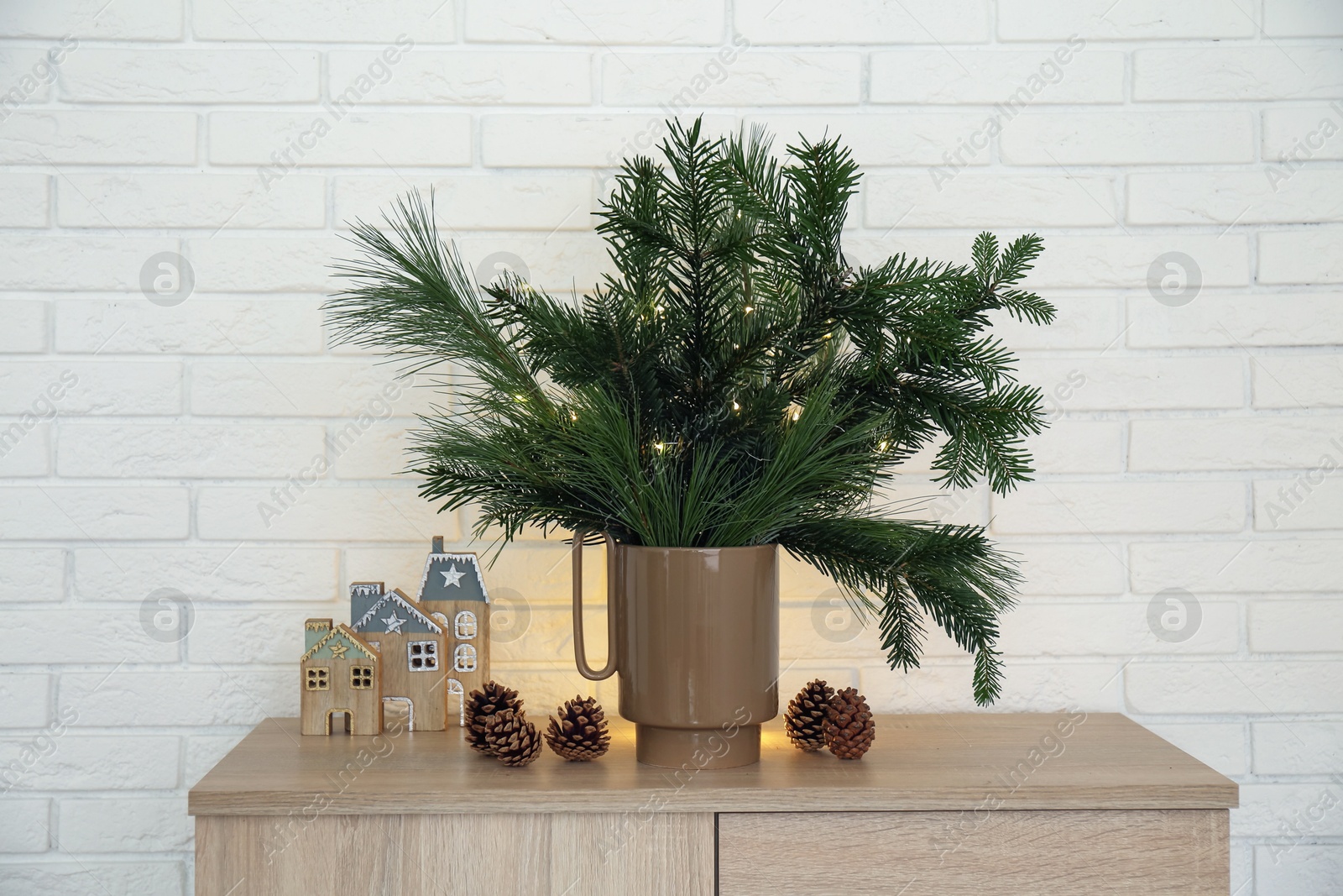 Photo of Beautiful Christmas composition of decorated fir and pine tree branches on wooden nightstand near white brick wall