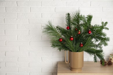 Photo of Beautiful Christmas composition of decorated fir and pine tree branches on wooden table near white brick wall, space for text