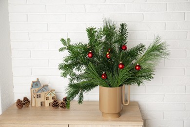 Photo of Beautiful Christmas composition of decorated fir and pine tree branches on wooden nightstand near white brick wall