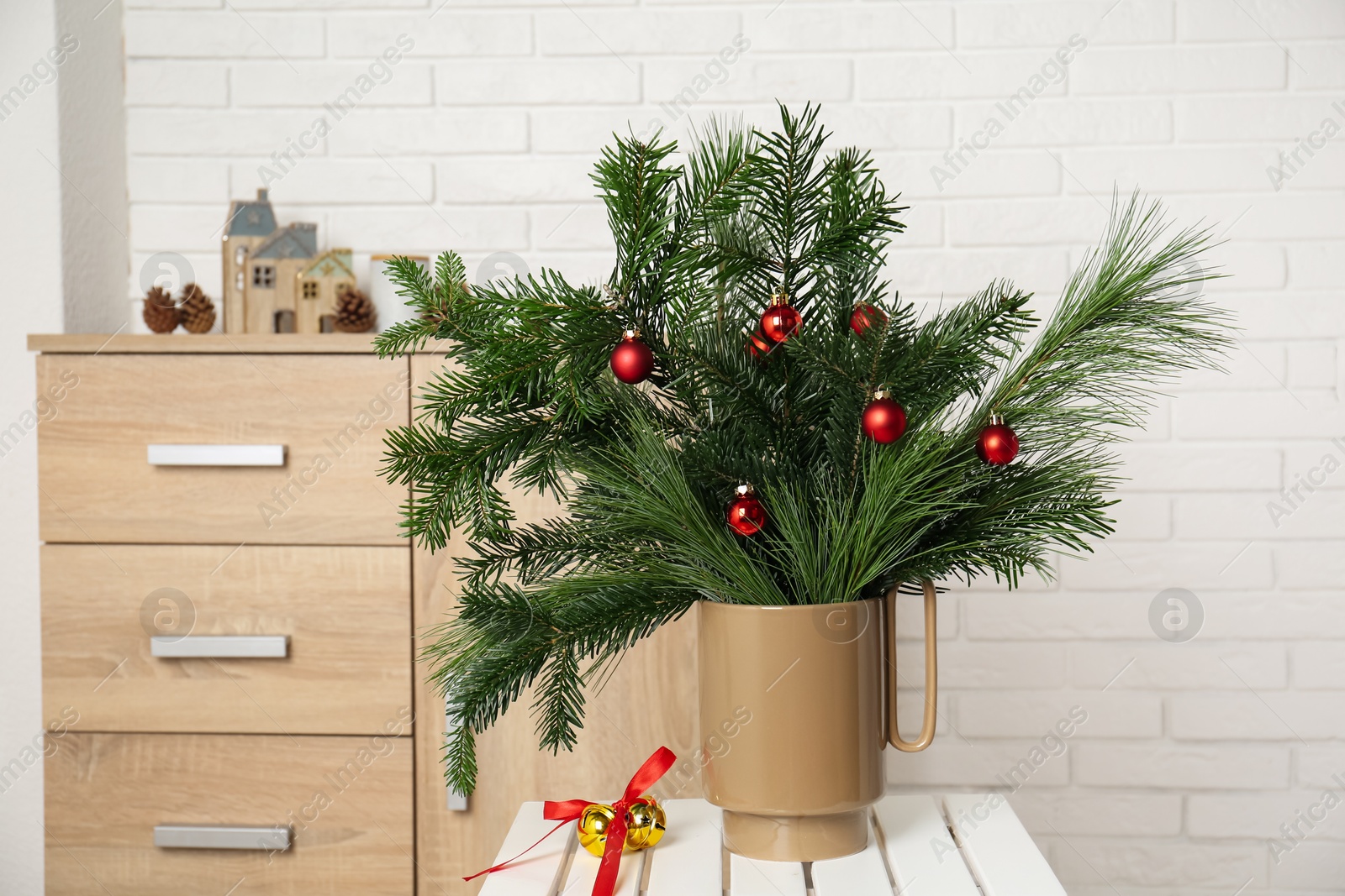 Photo of Beautiful Christmas composition of decorated fir and pine tree branches on stool at home